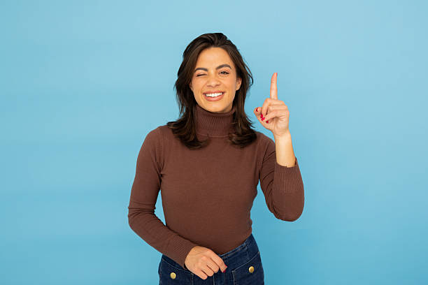 istock Cheerful woman winking, pointing upward near blue studio backdrop, expressing playful confidence with energetic pose 2217095627
