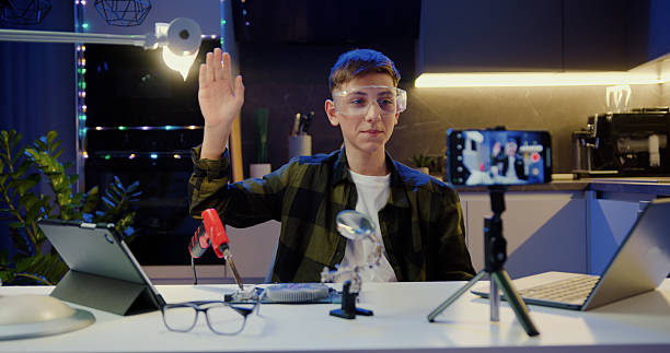 istock Smart teenage schoolboy vlogger makes online streaming using smartphone teaches to work with soldering and tools. Teenage boy recording his video blog in evening at home. 2217096300