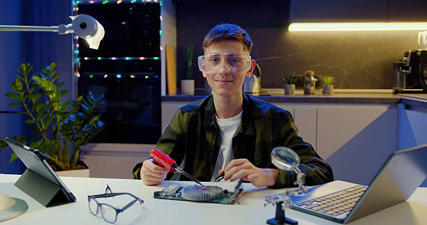 istock Attractive, smiling, satisfied, skilled, boy, protective, glasses, looking, camera, gesturing, ok, during, soldering, special, panel, using, iron, evening, home. 2217096867