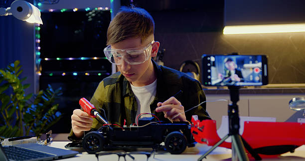 istock Focus on screen of smartphone. Schoolboy vlogger makes online streaming using smartphone teaches to work Boy repairing his remote controlled toy car with a tool in hand and carefully assembles toy car with screwdriver. 2217098667