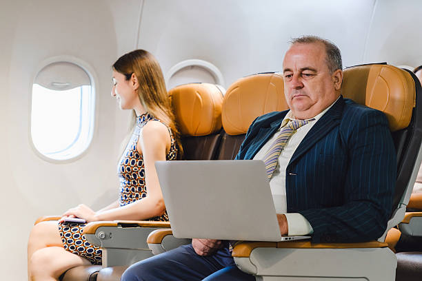 istock Businessman using onboard WiFi on a laptop while flying, seated beside a relaxed female passenger. Highlights inflight connectivity, digital services, and productivity in modern air travel. 2217107771