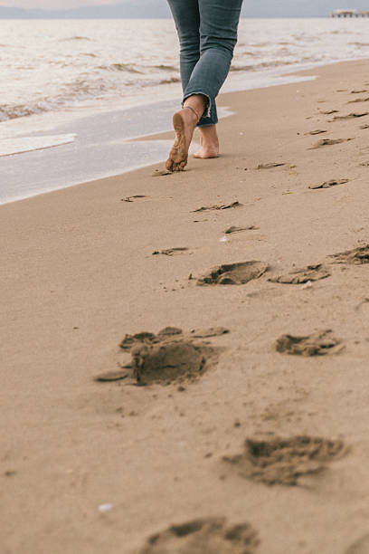 A serene moment captured as a person walks barefoot along the beach, leaving a trail of footprints in the sand. The ocean waves gently lap at the shore, conveying a sense of peace and relaxation
