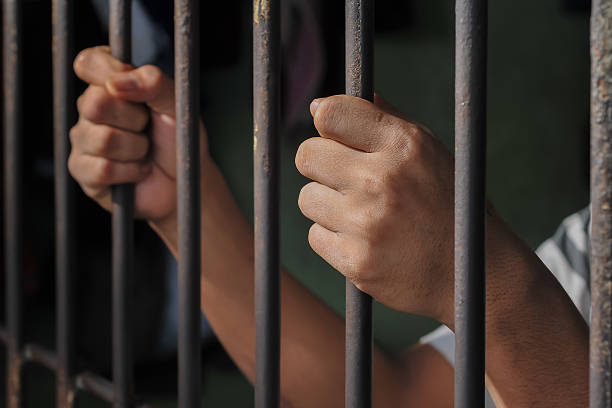 istock hands of a prisoner behind prison bars on black background 2217111993