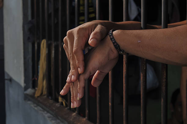 istock hands of a prisoner behind prison bars on black background 2217112007
