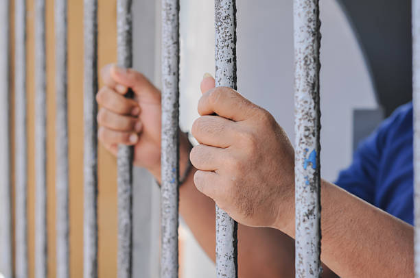 istock hands of a prisoner behind prison bars on black background 2217112024