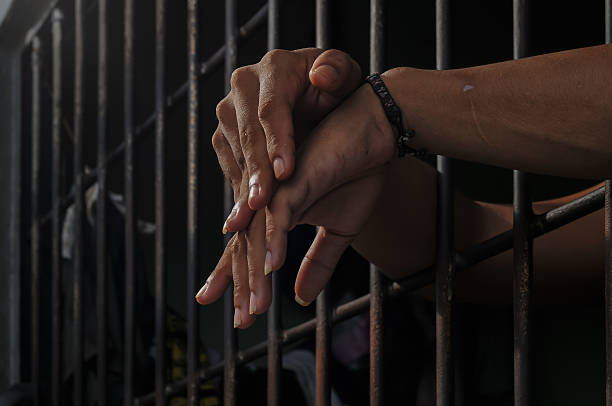 istock hands of a prisoner behind prison bars on black background 2217112031