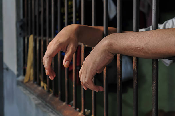 istock hands of a prisoner behind prison bars on black background 2217112192