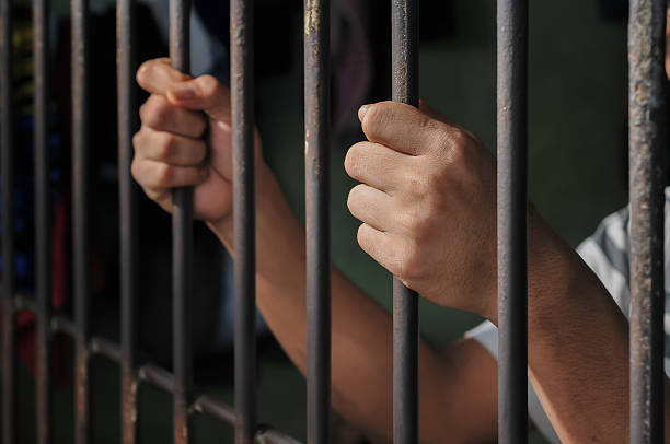 istock hands of a prisoner behind prison bars on black background 2217112388