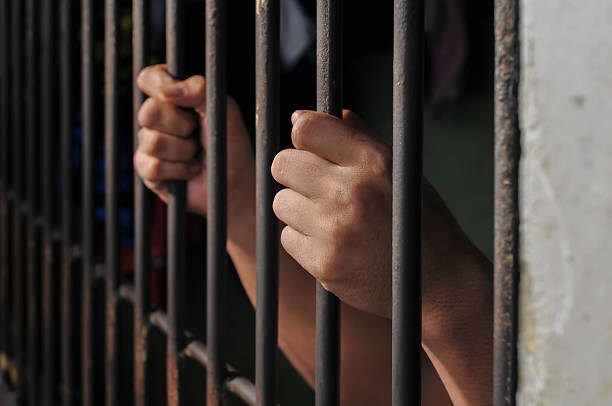istock hands of a prisoner behind prison bars on black background 2217112396