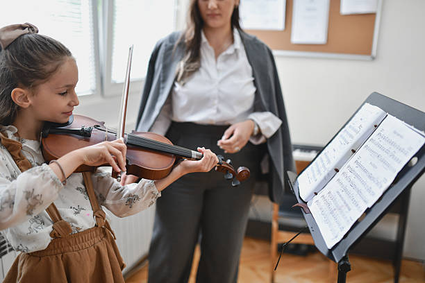 istock Cute Girl Having Playing Violin Piece While Teacher is Standing Near Her 2217112585