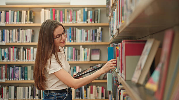istock Female student browsing books in a university library holding a tablet. 2217114402
