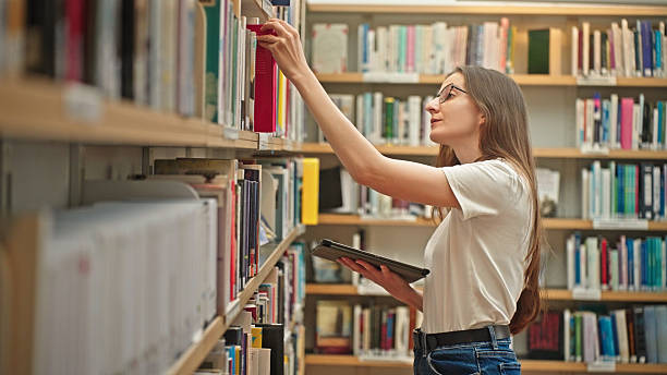 istock Female student browsing books in a university library holding a tablet. 2217114473