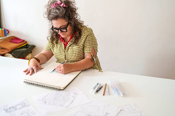 Mid adult woman sketching a detailed table design in her workshop, showcasing her creativity and skill as a furniture designer