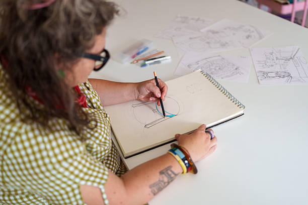 Woman wearing glasses sketching a design for a table in her workshop, focused on creativity and craftsmanship while working on her project