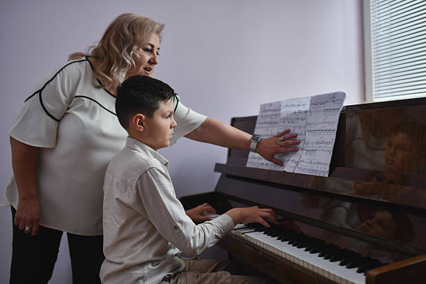 istock Teacher Gesturing Toward Left-Hand Section As Boy is Playing Piano With Determination 2217115235