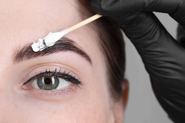 istock Brow lamination. Cosmetologist applying cream onto woman's eyebrows, closeup 2217118436