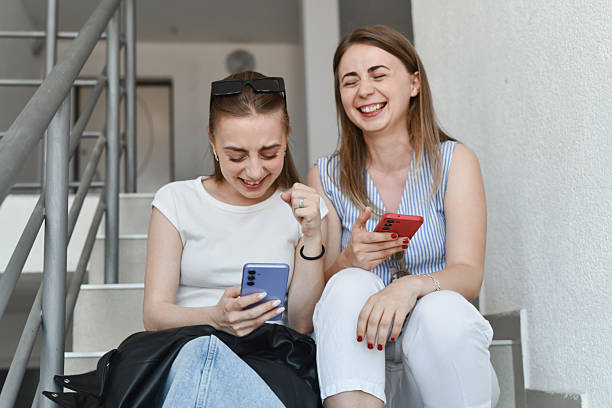 istock Happy Sisters Reacting To Day Trading Success Notification While Sitting on Stairs 2217122967