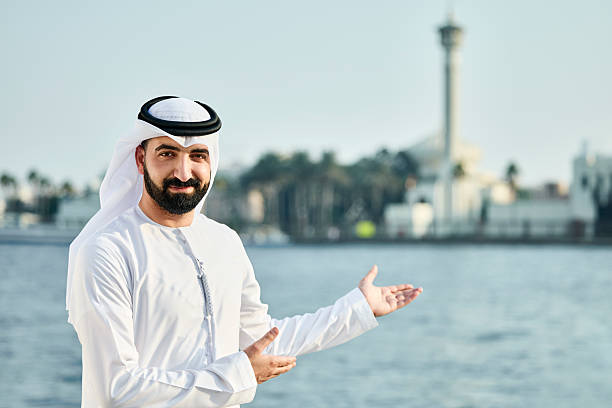 Portrait of smiling Saudi male gesturing at sunny day. Muslim man in traditional clothes. He is standing near sea.