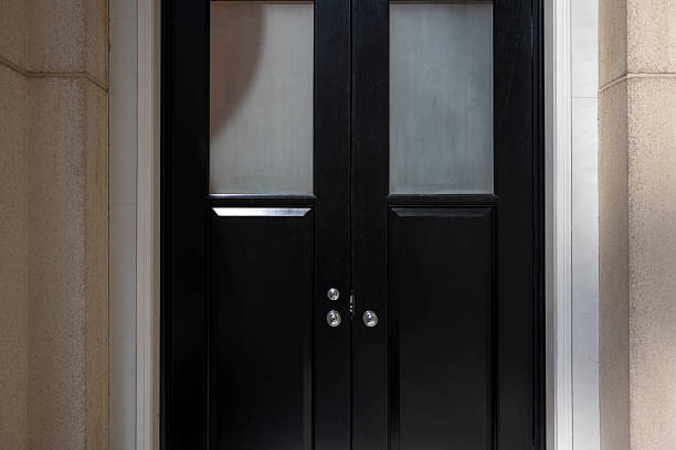 A black door with frosted glass panels set within a stone wall, creating an elegant entrance. The visual style is modern and minimalist, evoking a sense of sophistication and privacy. Potential usage includes architectural design inspiration or interior decoration concepts.