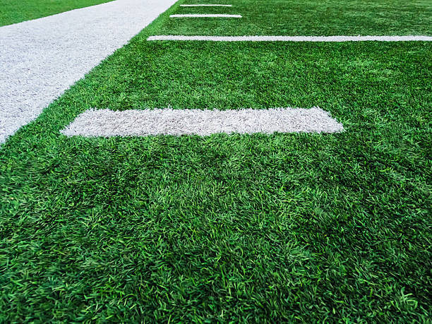 Bright green turf football field surface with white sidelines and yard line markings. Overhead view.
