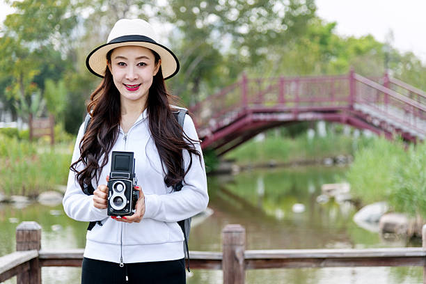 Woman taking photos with a vintage camera in park.