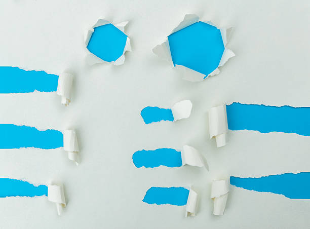 istock Tear holes in white paper to expose the blue background 2217145571