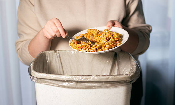 istock Woman throwing away food leftovers into garbage bin trash. Scraping food with spoon. Compost from leftover food. Environmentally responsible, reducing pollution. 2217145791