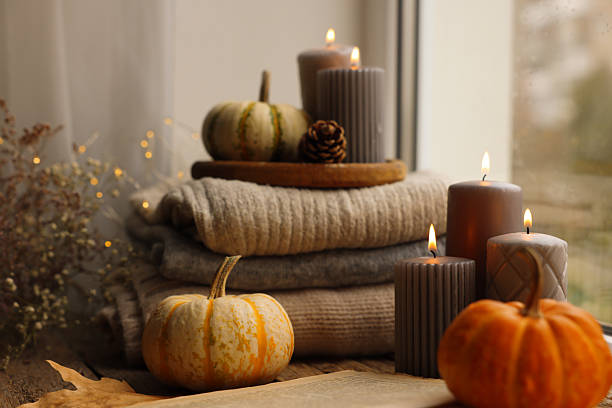 istock Burning candles, open book and stack of soft sweaters on windowsill. Autumn atmosphere 2217146354
