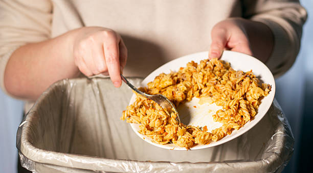 istock Woman throwing away food leftovers into garbage bin trash. Scraping food with spoon. Compost from leftover food. Environmentally responsible, reducing pollution. 2217146533