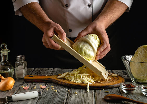 istock A chef skillfully shreds cabbage with a mandoline on a wooden cutting board. Ingredients are neatly arranged, showcasing the process of food preparation in a cozy kitchen atmosphere 2217149128