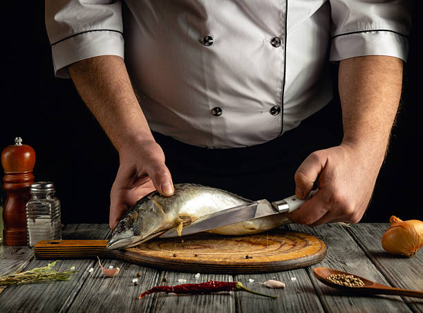 istock A skilled chef expertly slices a whole fish on a wooden cutting board in a warm kitchen. Various ingredients and seasonings are arranged nearby, creating an inviting atmosphere 2217149132
