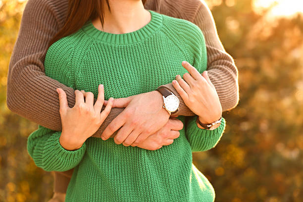 A happy couple embraces fully near a tranquil pond scene, with the woman in a red jacket and the man in a yellow shirt, capturing a heartfelt moment of joy and connection.