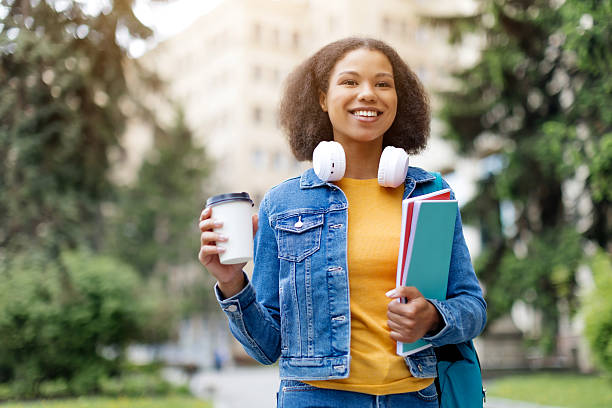 istock Smiling student woman outdoors with takeaway coffee cup and books in hands 2217160877