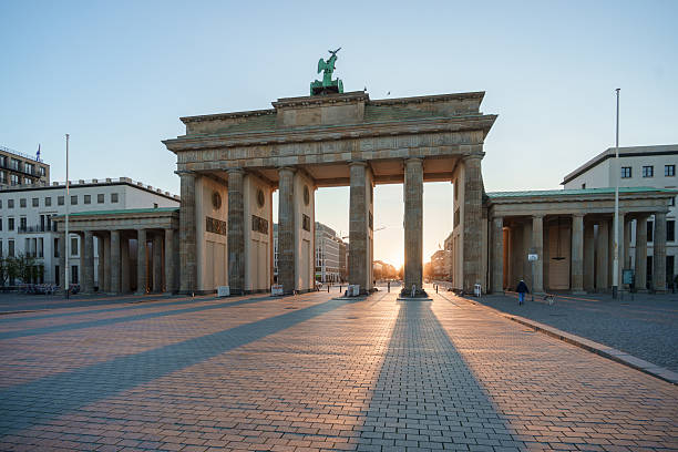 istock The Brandenburg Gate in Berlin at sunrise, casting long shadows on the empty square with soft golden light illuminating the historic monument 2217162021