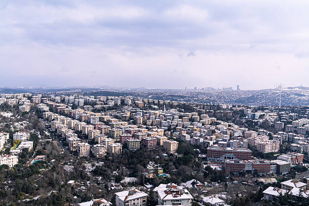 This panoramic view captures the dense urban fabric of Istanbul, showcasing a vast landscape of residential building structures covering the city's hills. The sheer scale and variety of the architecture highlight the ongoing challenges and realities of urban transformation and renewal in a major metropolis. The snow-covered rooftops unify the diverse building stock, offering a unique perspective on housing density, city planning, and the architectural evolution of one of the world's most dynamic cities