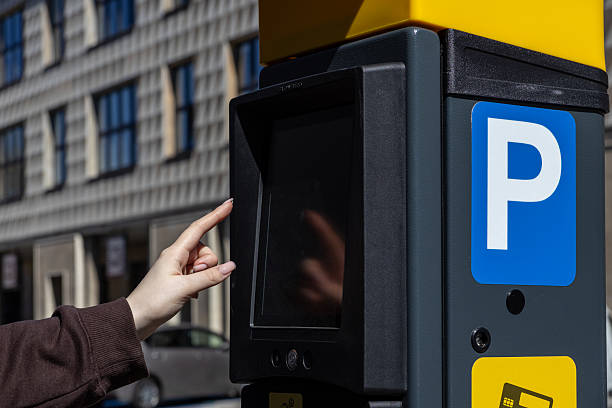 istock Female hand using touchscreen parking meter terminal on city street in bright daylight, close-up with blue parking symbol 2217174712