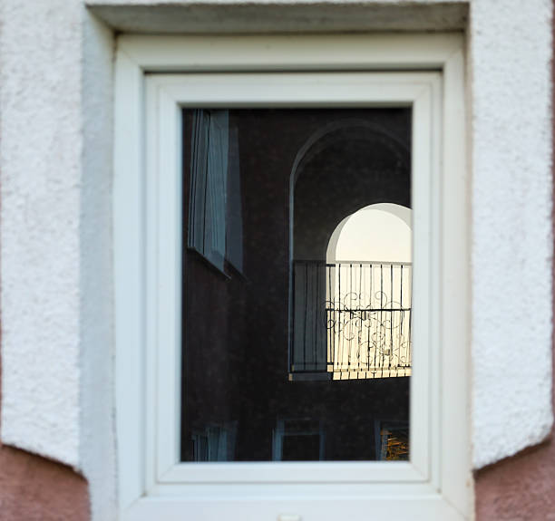 The reflection of an arch with a balcony in the window creates an interesting optical illusion. Light from the balcony highlights its wrought-iron railings, adding elegance.