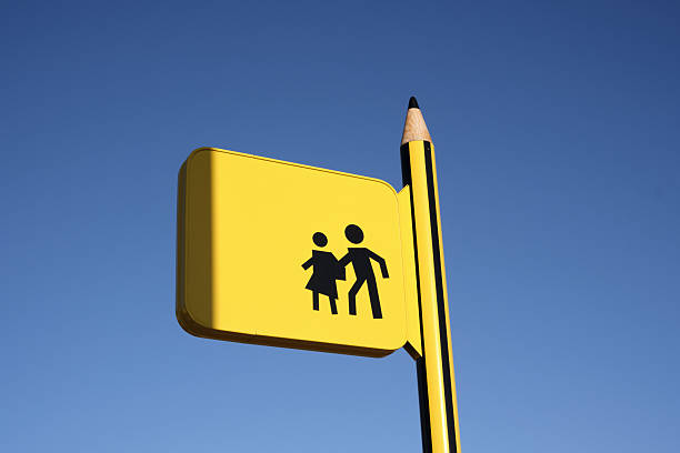 School crossing sign with pencil-shaped post against blue sky.