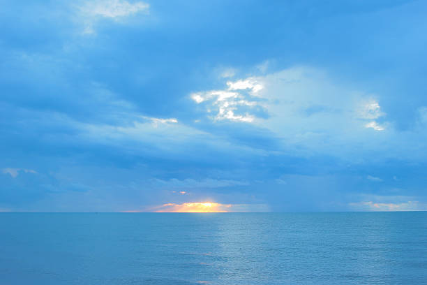 Serene sunrise over the calm sea , with golden sun rays piercing through a gap in the clouds.