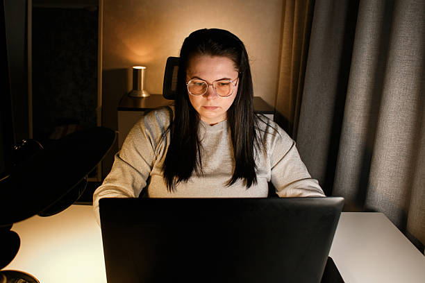 istock Woman working on laptop late evening at home. Concentrated female employee solves work issues sitting at computer at work desk. 2217182031