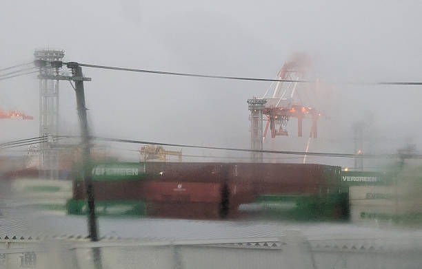 Osaka, Japan - April 14, 2025: Freight traffic on Yumeshima Island, at the major port of Osaka. Gantry cranes and shipping containers stand through the rain and wind on a spring afternoon.