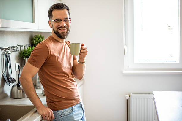 istock Young man smiling and drinking coffee in kitchen 2217191680