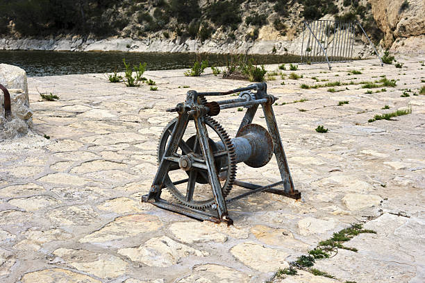 Rustic metal winch on stone pavement by a lakeside.