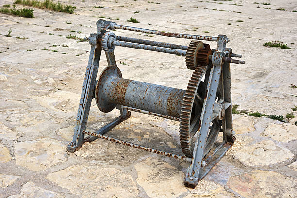 Rusty industrial winch on weathered stone surface with gears and mechanism detail.