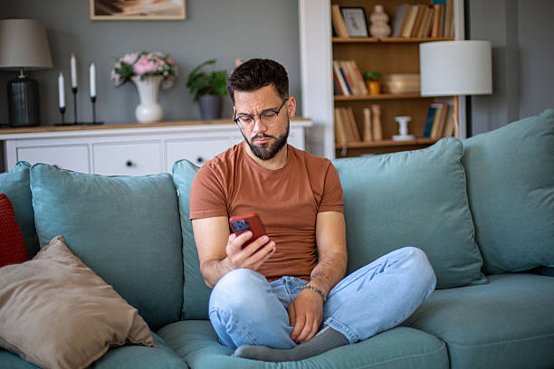 istock Young man is using mobile phone while sitting on sofa in living room 2217193970