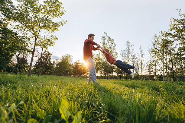 Father spinning son in park at sunset