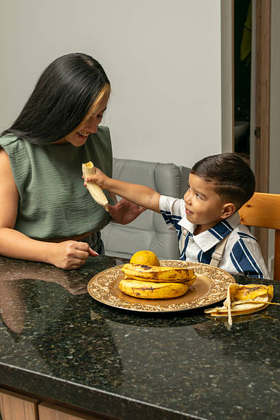 Mother and Son Sharing a Banana at a Kitchen Table – Family Bonding, Healthy Eating, Parental Nourishment Concept