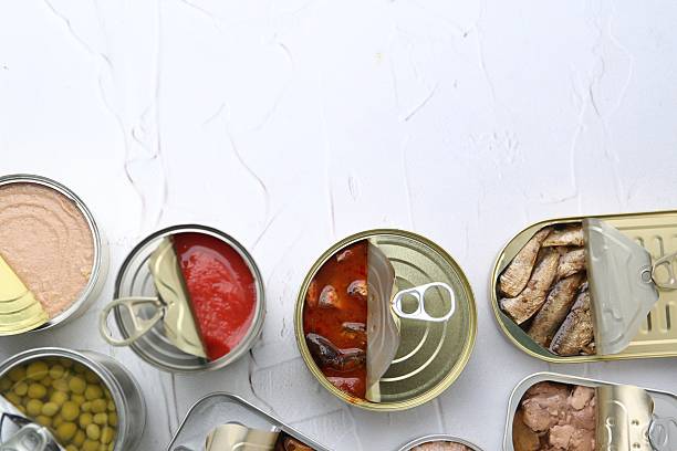 istock Open tin cans with different preserved products on white table, flat lay. Space for text 2217199037