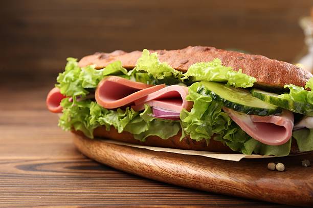 istock Delicious baguette sandwich with ham on wooden table, closeup 2217199219
