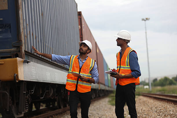 istock Two Indian logistic staff with safety jacket and PPE check container on rail transportation ,World wide logistic, The container cargo shipment by rail transportation , Logistic manager and staff working check container on rail way 2217202040